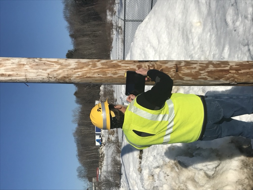 Utility crew capturing field data on a tablet at a pole